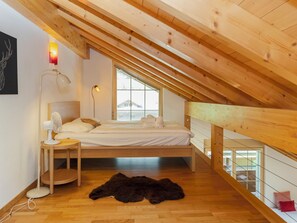 A bedroom with a sloped ceiling, a bed, a desk, a chair, a lamp, and a window. - Staubbach by Interhome (Lauterbrunnen)