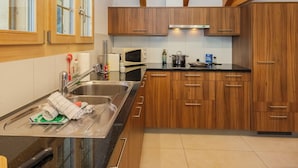 A modern kitchen with wooden cabinets, a stainless steel sink, a microwave, and a stove. - Staubbach by Interhome (Lauterbrunnen)