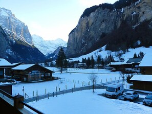 A snow-covered mountain village with buildings and parked cars.