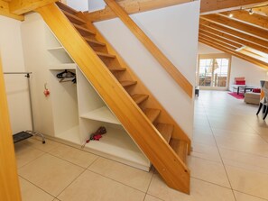 A wooden staircase in a modern interior with a tiled floor and a view of a living area.