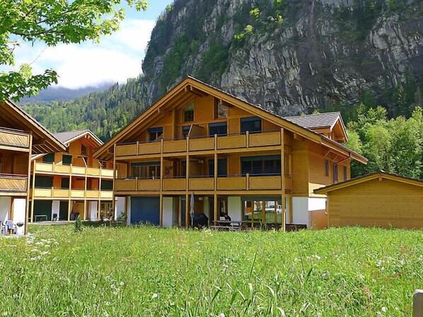 A multi-story wooden building with balconies, set against a mountainous backdrop.