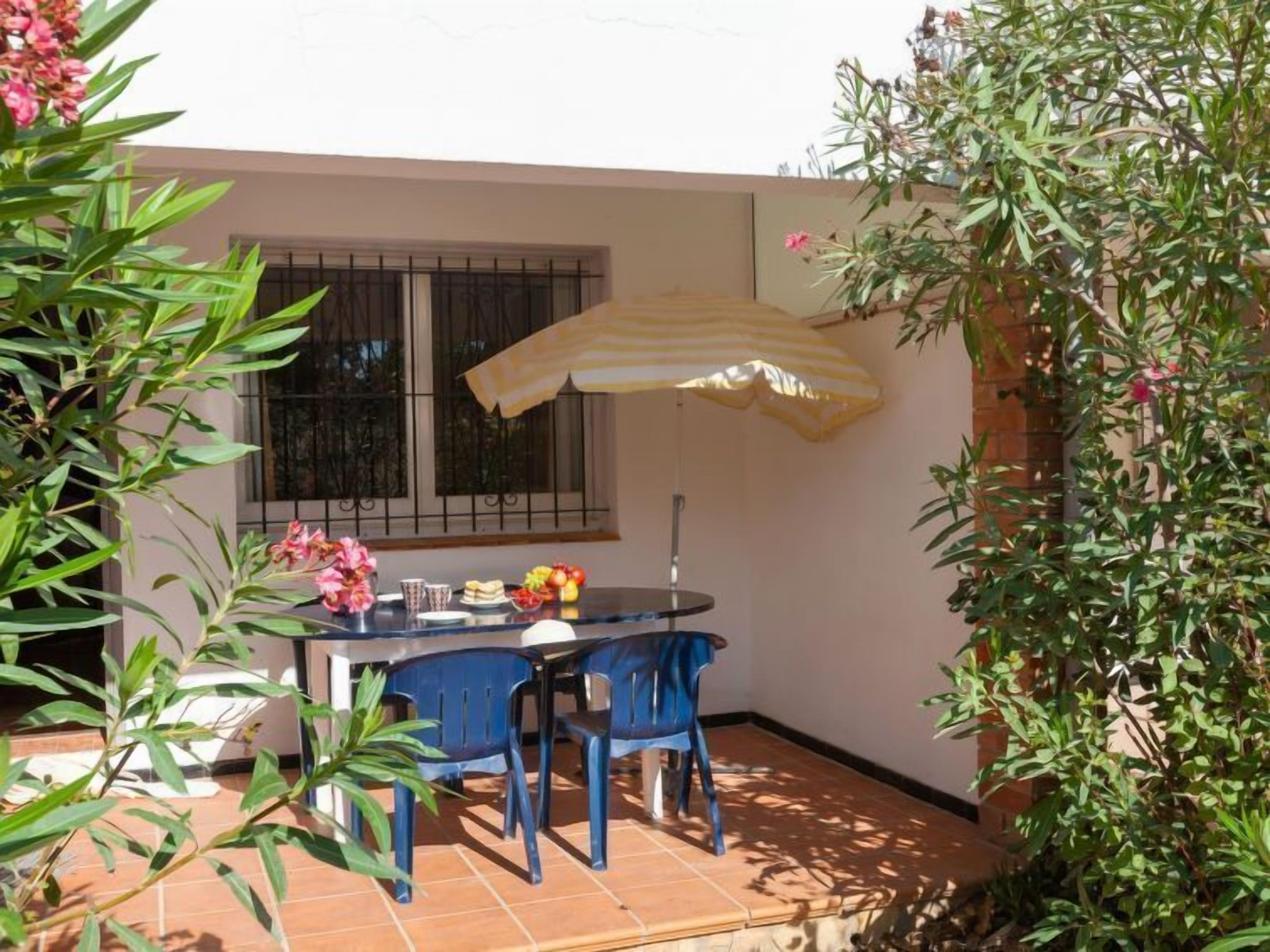 A patio with a table and chairs, a window with bars, and a yellow umbrella.