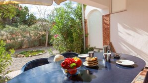 Un área de comedor al aire libre con una mesa dispuesta para dos personas, un frutero y una cafetera.