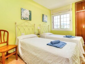 Una habitación de hotel con dos camas, una silla de madera y un ventanal con cortinas.