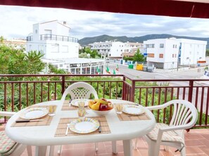 Un balcón con una mesa dispuesta para dos personas, con vistas a una calle flanqueada por edificios y montañas al fondo.