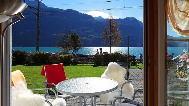 A room with a view of a lake and mountains, a round table, and two chairs.