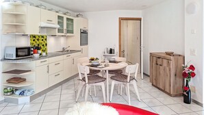 A compact kitchen with white cabinets, a microwave, and a dining area with a table and chairs.