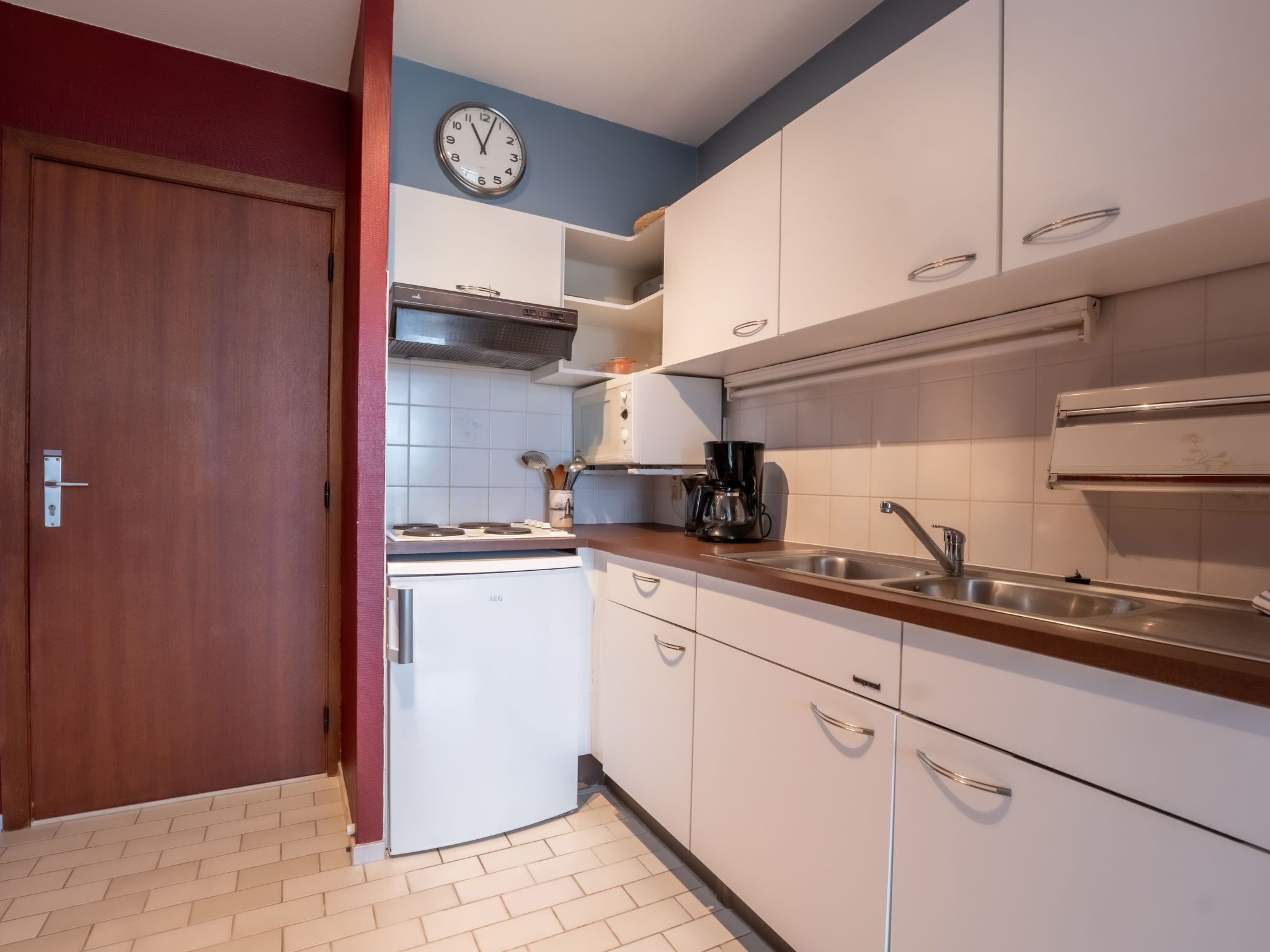 Una cocina compacta con armarios blancos, un lavamanos de acero inoxidable, un microondas y una estufa.