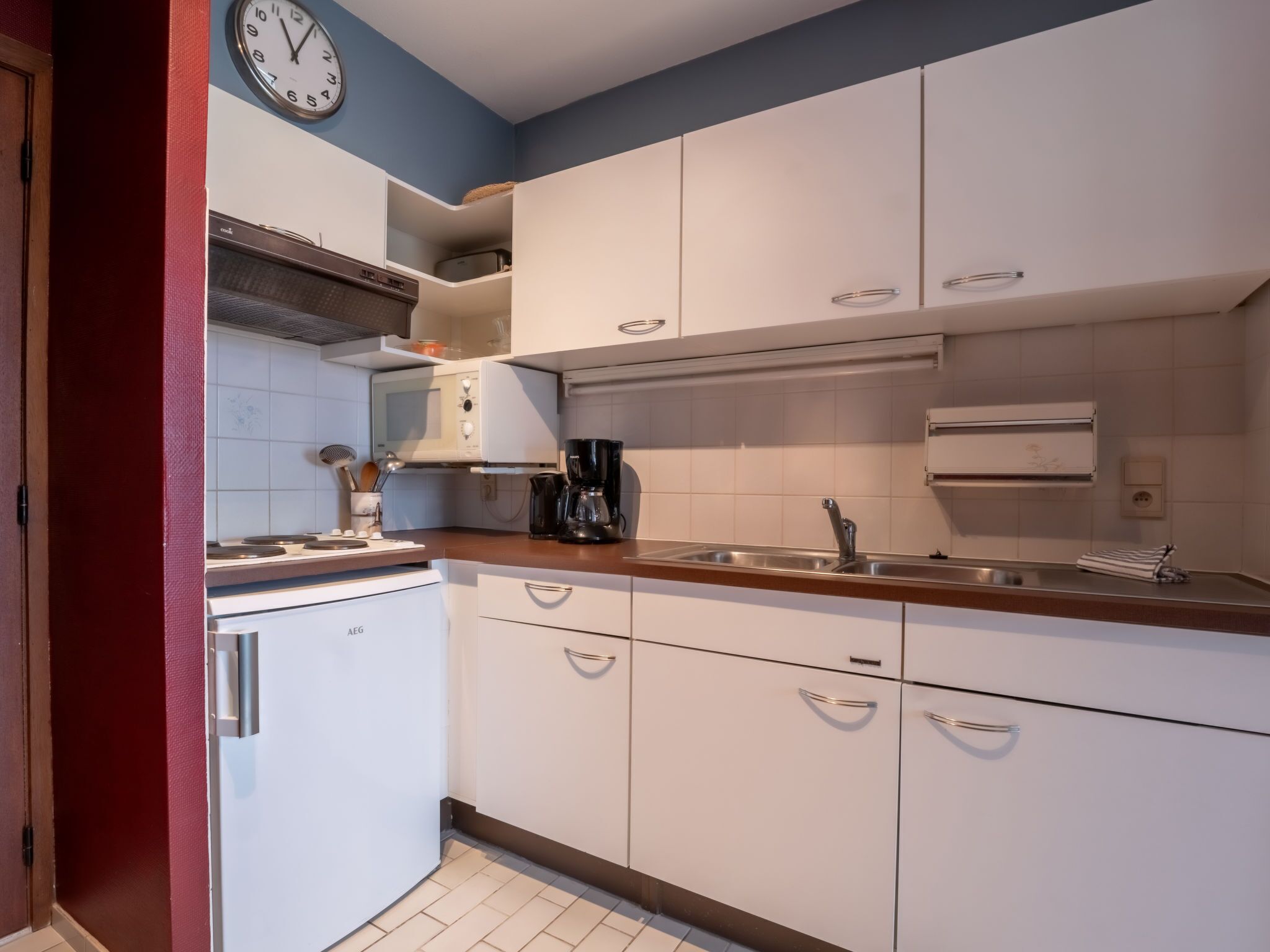 A compact kitchen with white cabinets, a stainless steel sink, and a microwave.