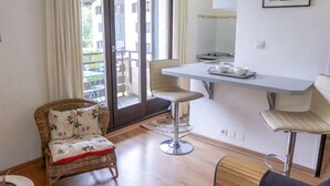 Ein modernes Wohnzimmer mit einem Korbstuhl, einer Essecke mit Barhocker und Blick auf einen Balkon mit Gartenmöbeln.