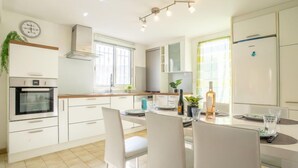 Una cocina moderna con armarios blancos, horno empotrado y comedor con mesa para dos.
