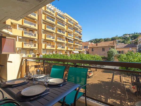 Ein Balkon mit Esstisch, der auf einen Wohnbereich mit einem gelben Gebäude und einer Hügelkulisse im Hintergrund blickt.