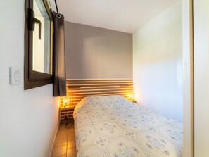 Ein Schlafzimmer mit einem Bett, einem Nachttisch mit Lampe, einem Fenster mit Vorhängen und einem an der Wand montierten Thermostat.