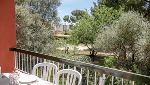 Ein Balkon mit Tisch für Zwei, der auf einen Garten mit Bäumen und ein Gebäude im Hintergrund blickt.