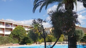 Ein Schwimmbecken mit Fliesen umgeben von Bäumen und einem mehrstöckigen Gebäude mit Balkonen.