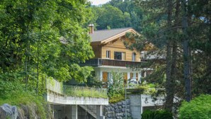 A two-story house with a stone facade, a wooden balcony, and a stone staircase leading to the entrance.