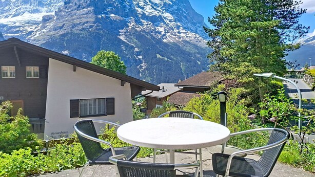 A mountain view with a building, outdoor seating, and a sign.