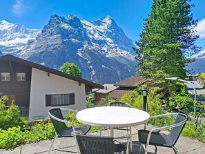 Vista de montaña con un edificio, asientos al aire libre y un letrero.