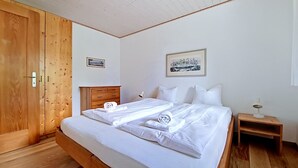 A bedroom with a wooden bed, a wooden wardrobe, a bedside table, and a wall-mounted picture.