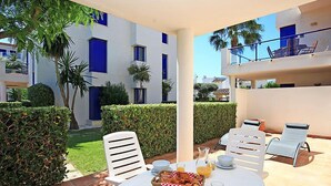 A patio with a table set for breakfast, surrounded by white chairs, and a view of a modern building with blue accents. - Alma del Sol by Interhome (Dénia)