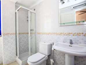 Et badeværelse med bruseniche, toilet og vask med spejl over.
