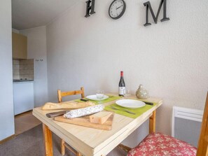 A dining area with a wooden table set for two, a bottle of wine, and a vase on the table.