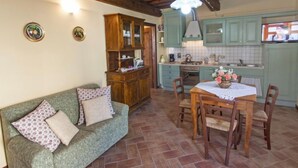 Ein gemütliches Wohnzimmer mit einer Couch, einem Esstisch mit Stühlen und einer Küchenzeile mit grünen Schränken und einer gefliesten Rückwand.