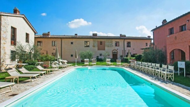 Ein rechteckiger Pool mit Liegestühlen und Sonnenschirmen, umgeben von Gebäuden im mediterranen Stil.