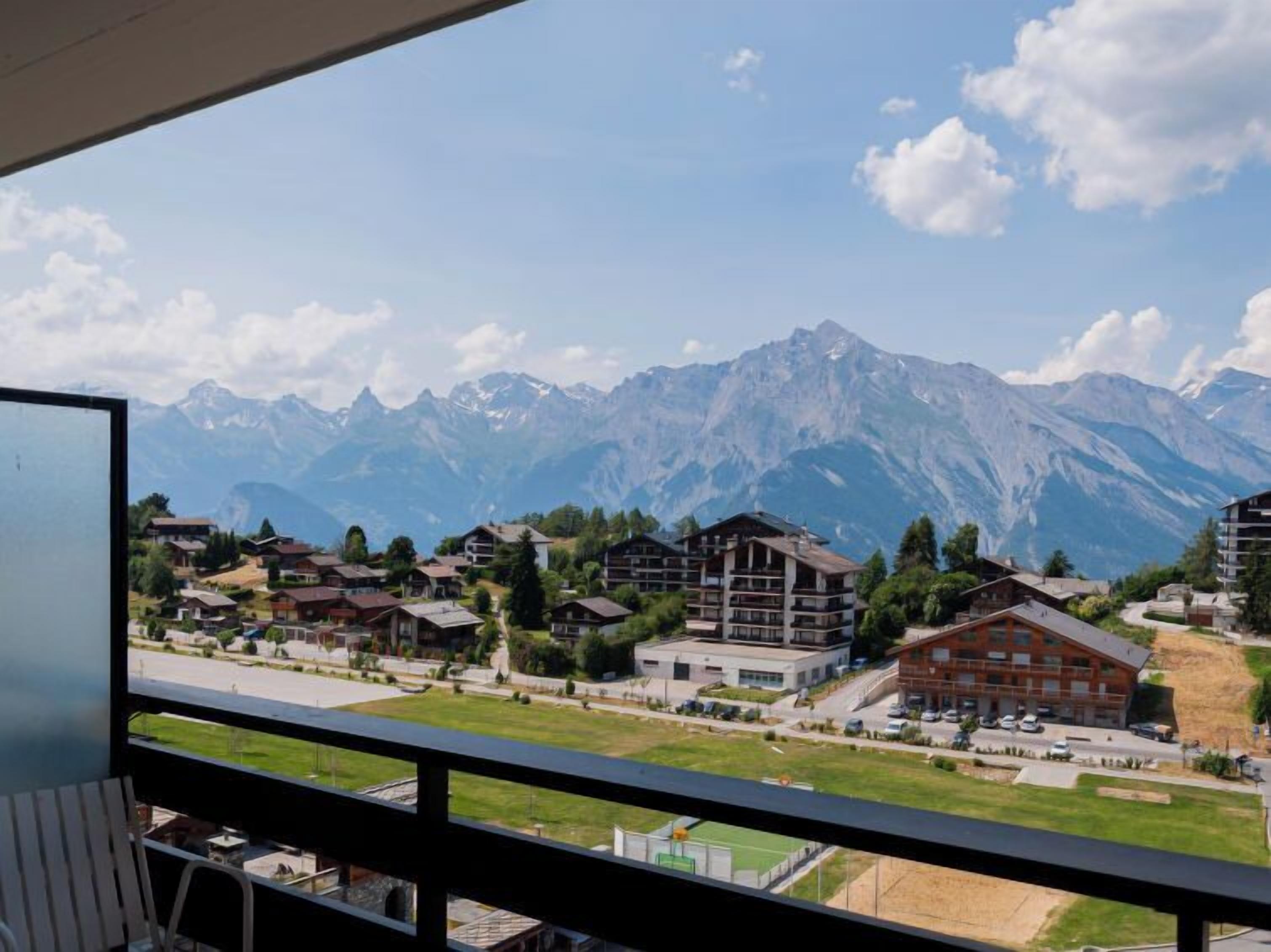 A mountain resort with chalet-style buildings, a parking area, and a view of snow-capped mountains.