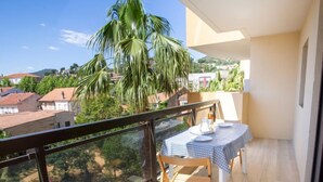Ein Balkon mit Tisch für zwei Personen, mit Blick auf eine Wohngegend mit Häusern und Palmen.