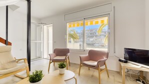 Een moderne woonkamer met een televisie, twee fauteuils, een bijzettafeltje en een potplant.