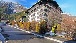 Un hôtel à plusieurs étages, doté de balcons, situé dans une région montagneuse où le sol est recouvert de neige et où les arbres arborent les couleurs de l’automne.