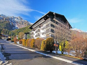A multi-story hotel with balconies, situated in a mountainous area with snow-covered peaks in the background.