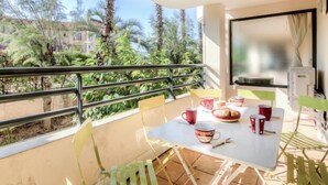 A balcony with a table set for two, chairs, and a view of greenery and buildings. - Le Magellan by Interhome (Saint-Raphaël)