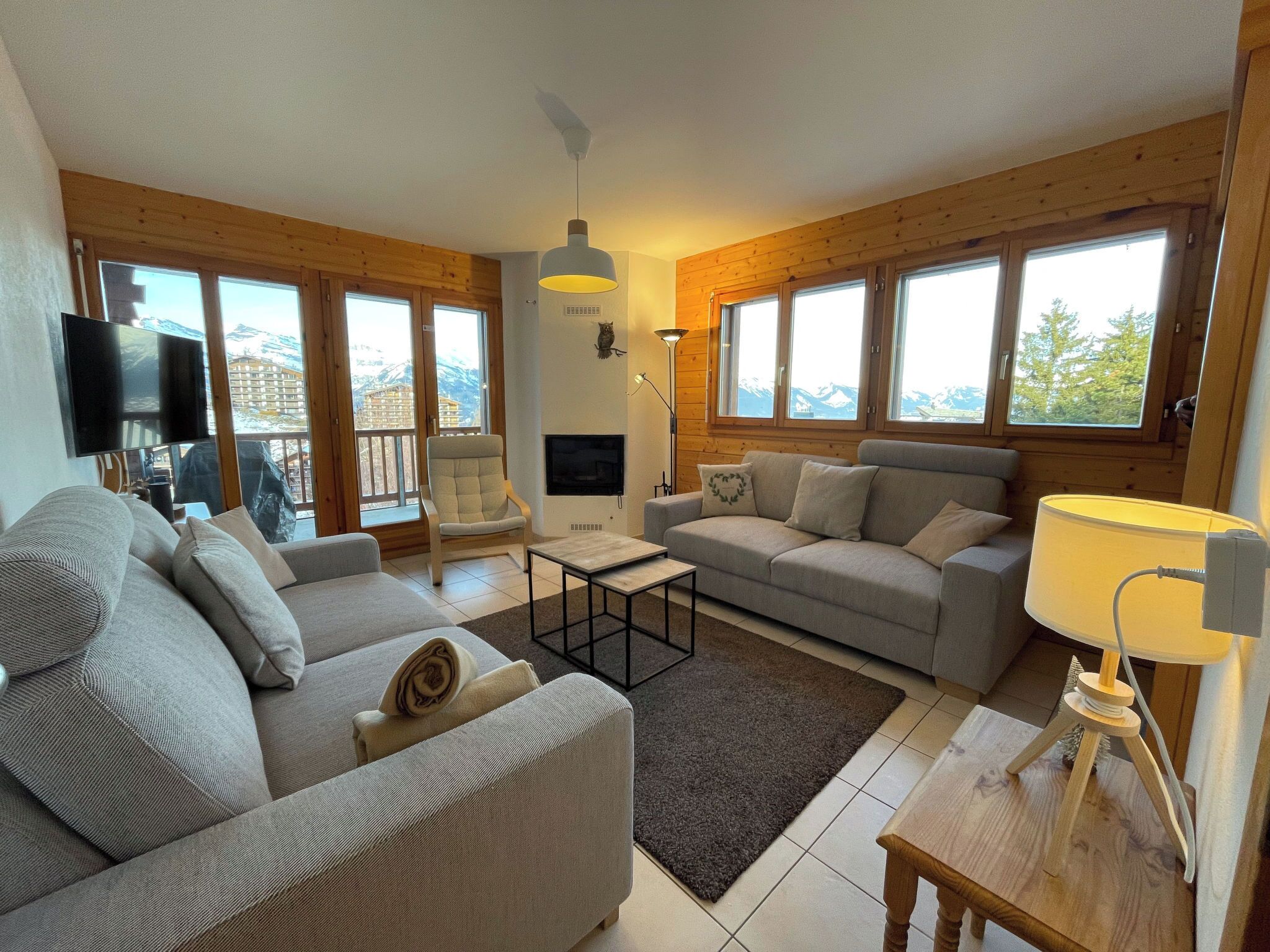 Una sala de estar con sofá, sillón y televisor. Cuenta con amplios ventanales y una chimenea.