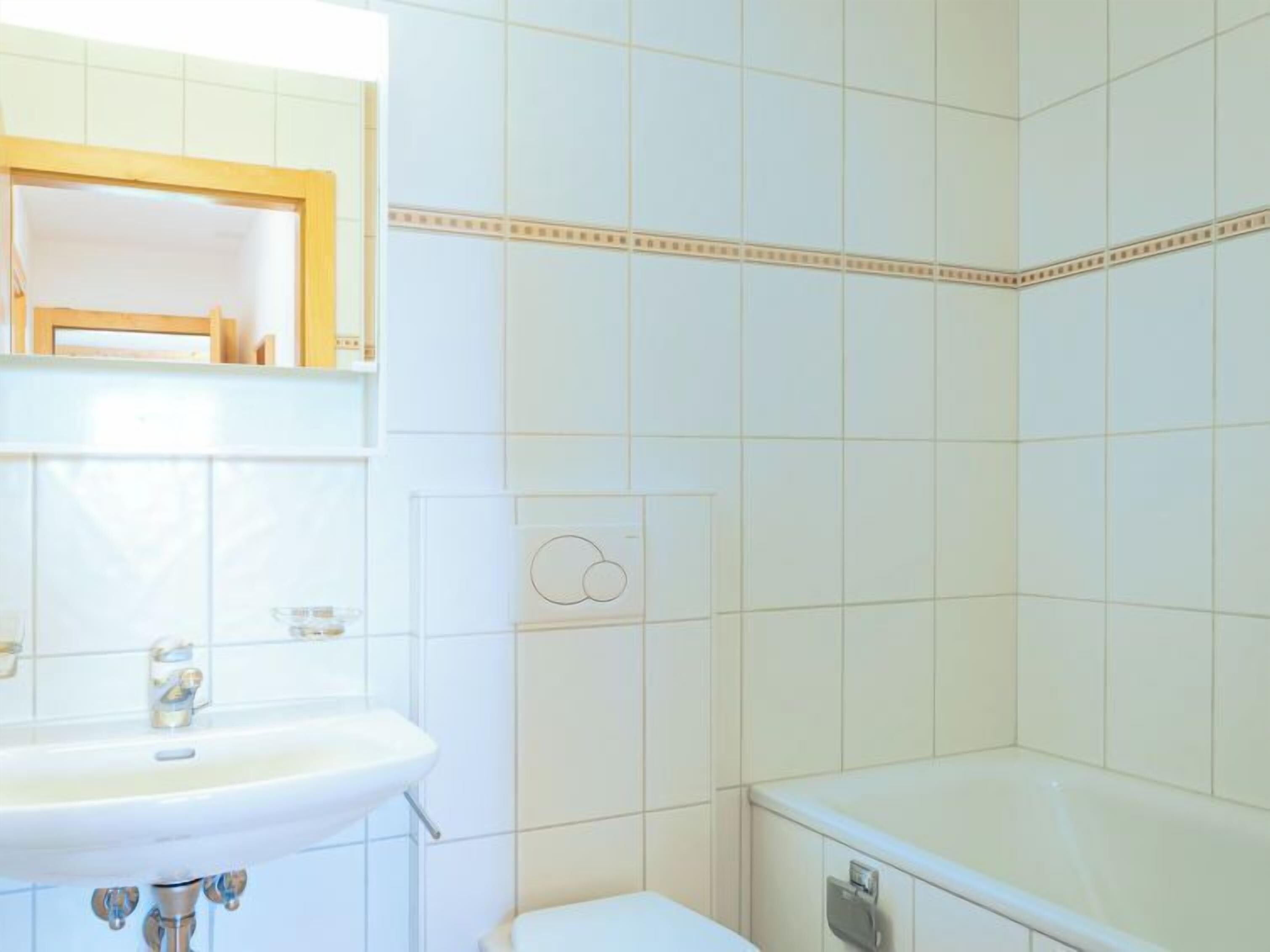 A bathroom with white tiles, a sink, a toilet, and a mirror.
