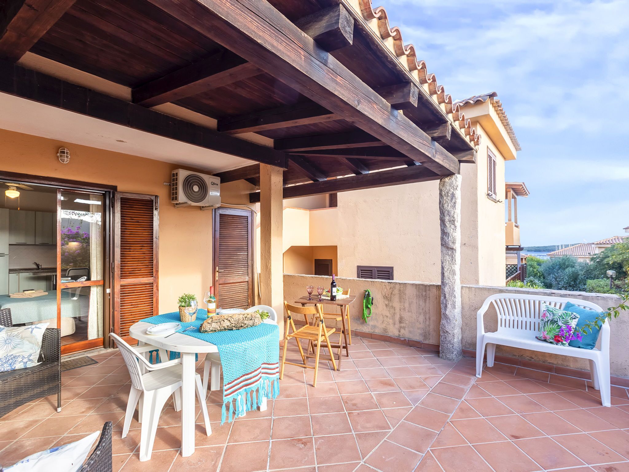 A covered patio with a table and chairs, a bench, and a view of the sea.