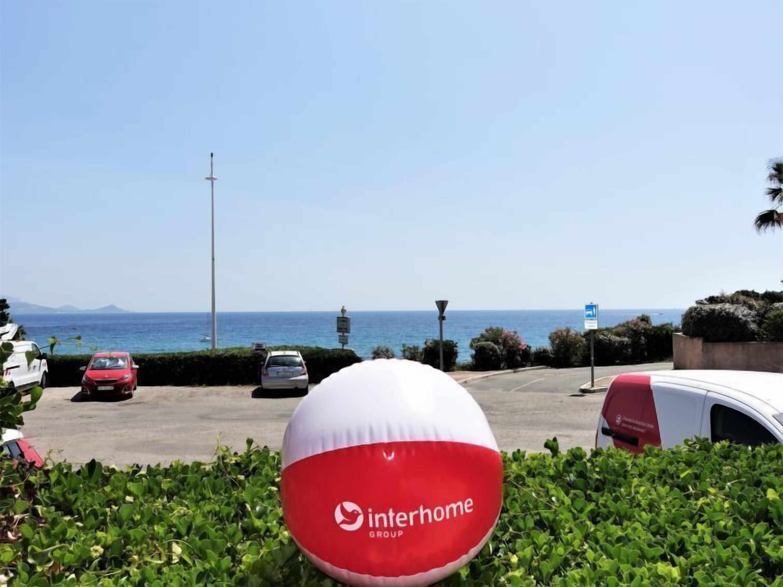 A parking area with a view of the ocean and a large inflatable ball with the Interhome Group logo.