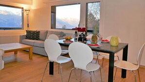 Una sala de estar moderna con un sofá, una mesa de comedor y sillas. Amplias ventanas ofrecen vistas a las montañas.
