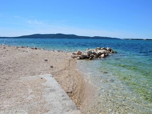 A beach with clear water, a rocky outcrop, and distant hills.