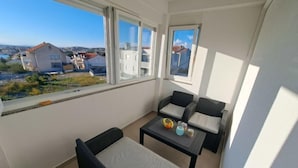 A balcony with a sofa and two chairs, a small table with a bowl of fruit, and a view of buildings and greenery. - Sun seeker by Interhome (Brodarica)