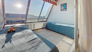 Ein kleiner Balkon mit Blick auf die Stadt, ein blaues Sofa, ein kleiner Tisch mit Spielzeug und ein gestreifter Sonnenschirm.