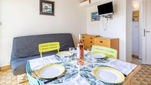 A dining area with a table set for four, a sofa, a television mounted on the wall, and a wooden loft above. - Hameau de Pech I by Interhome (Cap d'Agde)