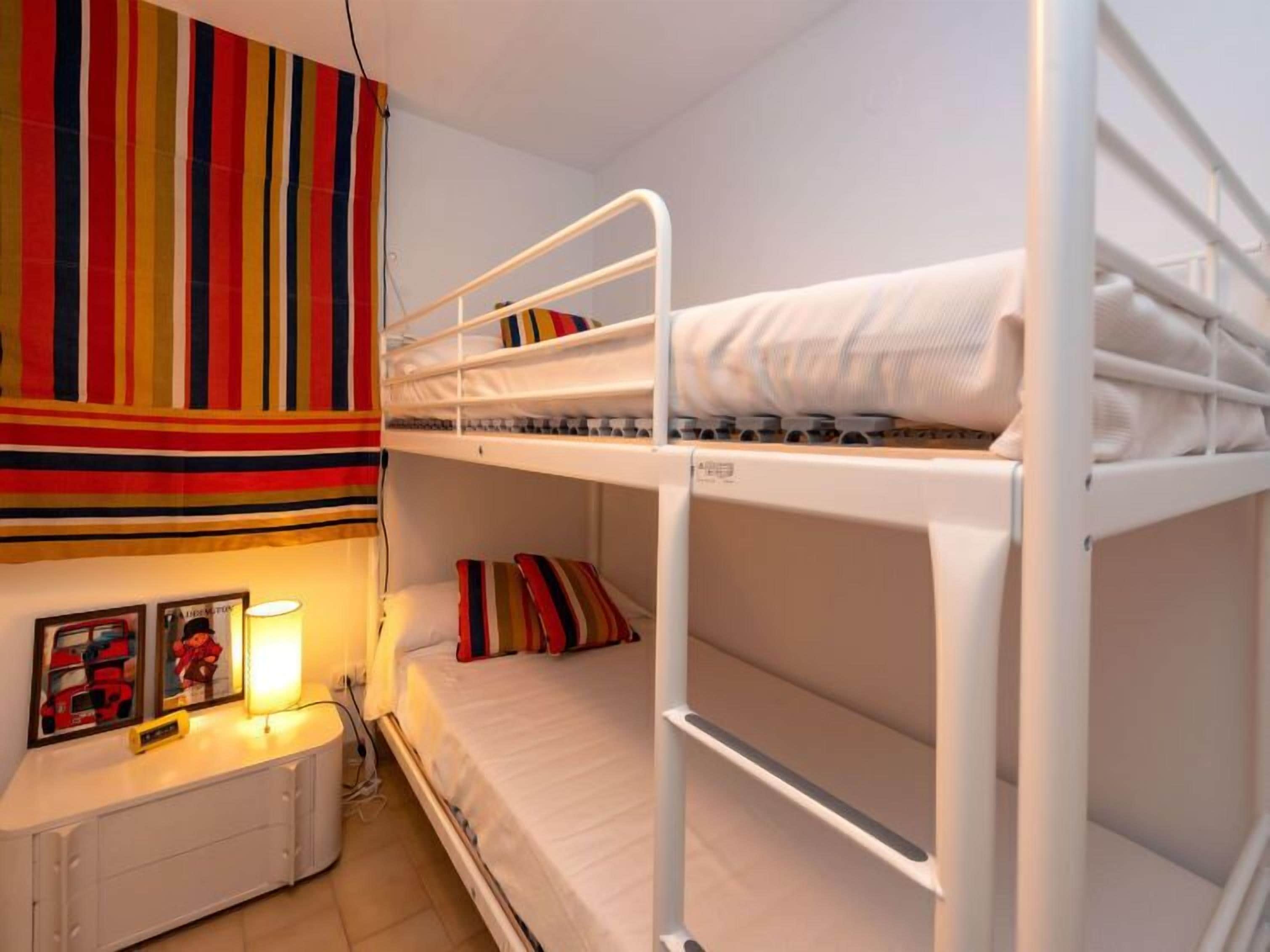 A bunk bed room with a striped curtain, a bedside table with a lamp, and framed pictures on the wall.