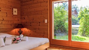 Habitación de cabaña de madera con una cama, una lámpara y un amplio ventanal corredero que da a un jardín.