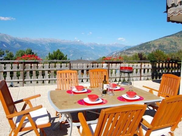 Una mesa para cuatro con sillas de madera, vista a las montañas y una valla de madera.