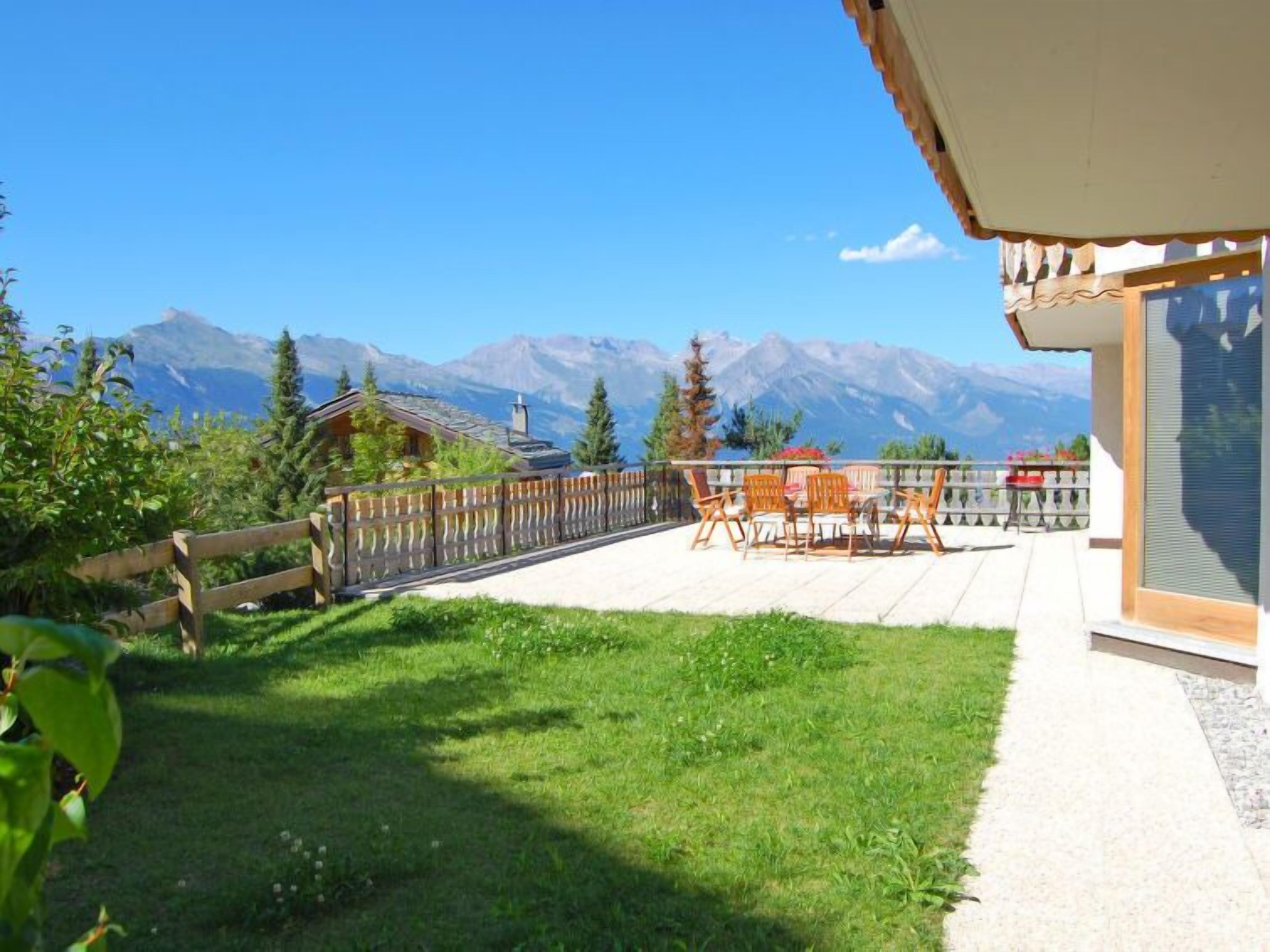 A patio with a table and chairs, a wooden fence, and a mountain view.