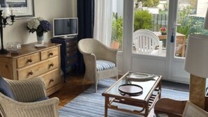 Un salon avec une table basse en bois, un canapé, un fauteuil, un téléviseur et un lustre.