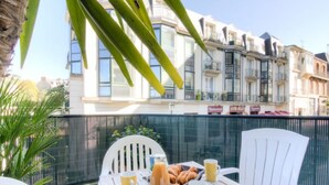 Une table avec des aliments pour le petit-déjeuner, deux chaises blanches et une vue sur des immeubles à plusieurs étages.