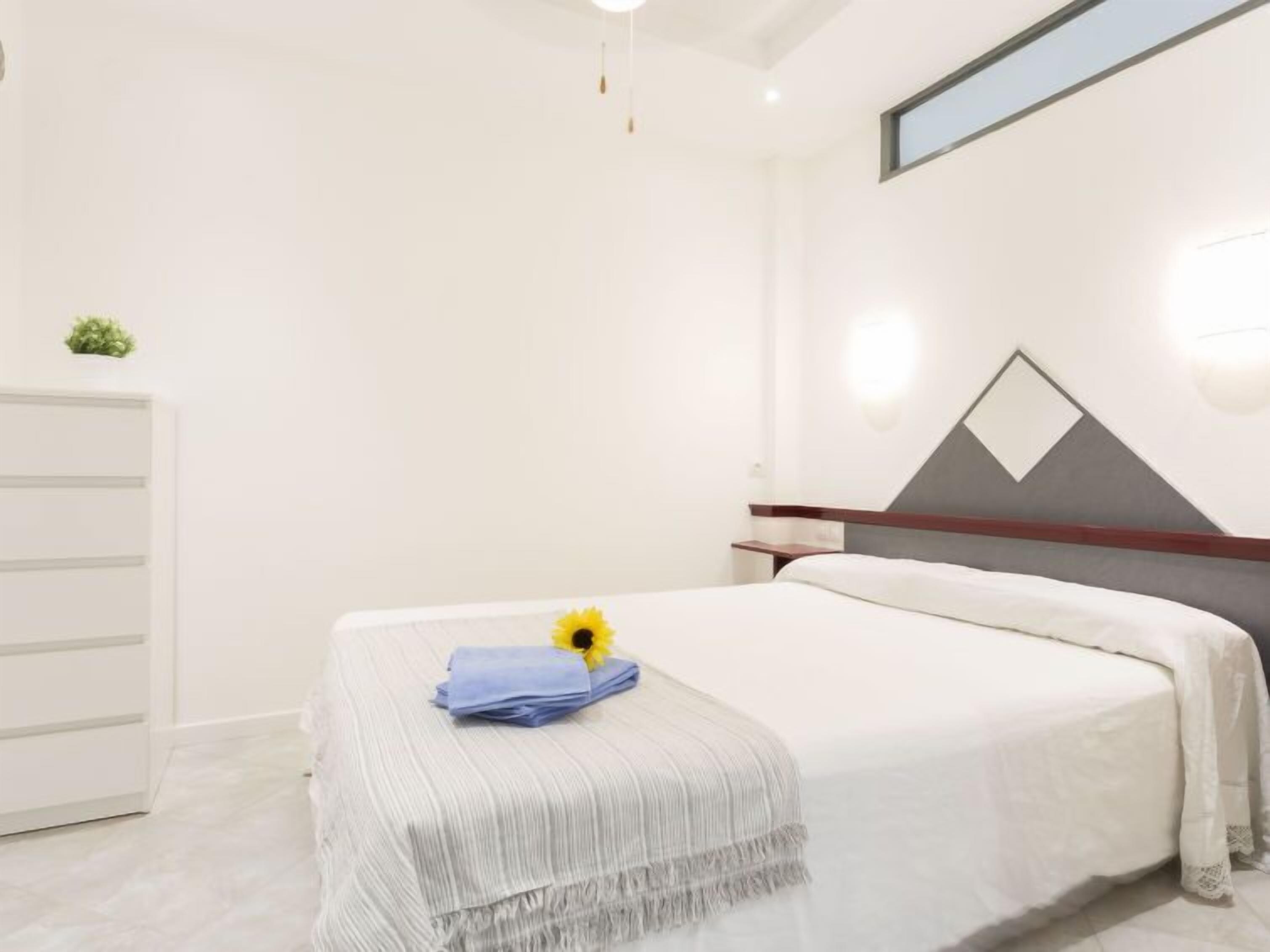 Une chambre d’hôtel moderne, équipée d’un lit, d’un petit bureau et d’un luminaire fixé au mur.